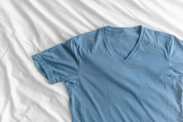 Blue simple t-shirt lie on white bed sheet.