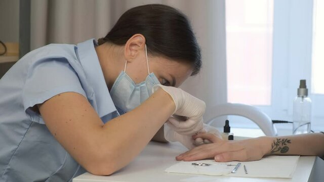 Classical manicure in salon, clinic, office. Hygiene and care for hands, beauty industry concept. Woman manicurist master cuts cuticle and skin on client's finger using tongs, side view.