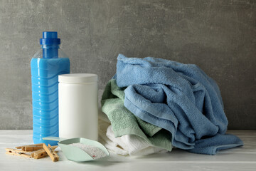 Detergent, powder and towels on wooden table against gray background