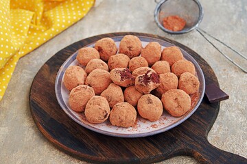 Homemade chocolate candy truffles on a dessert plate on a wooden board on a gray concrete background. Truffle candy recipes. Chocolate candies.