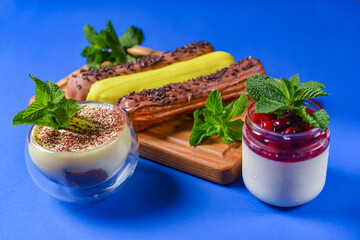 Different coloured eclairs on a wooden board over blue background, tiramisu and panna cotta dessert.