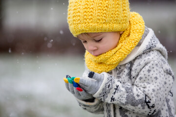 Beautiful blond toddler child, boy, with handmade knitted sweater playing in the park with first...