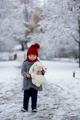 Beautiful toddler child, cute boy, playing in snowy park winter time