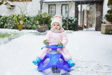 Cute little toddler girl enjoying a sleigh ride on snow. Child sledding. Baby kid riding a sledge in colorful fashion clothes. Outdoor active fun for family winter vacation on day with snowfall