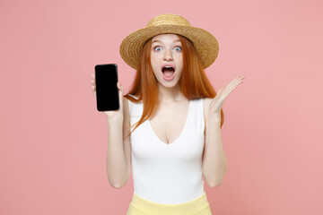 Young shocked surprised redhead woman in straw hat summer clothes hold texting mobile cell phone with blank screen workspace area spreading hands isolated on pastel pink background studio portrait