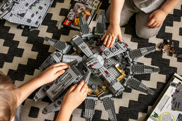 Fototapeta premium Two boys assemble the Millennium Falcon set from Lego according to the instructions. Nearby lies the spaceship Imperial Cruiser and the Death Star. Fans of the Star Wars movie.