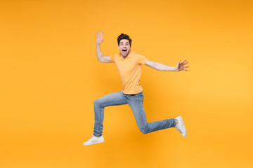 Fototapeta na wymiar Full length side view of young overjoyed caucasian excited fun surprised man 20s wearing casual basic t-shirt jeans high jumping up spreading hands isolated on yellow color background studio portrait.