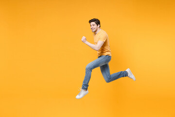 Fototapeta na wymiar Full length side view of young happy caucasian fun energetic sporty man 20s wear casual basic t-shirt jeans high jumping up running looking aside isolated on yellow color background studio portrait