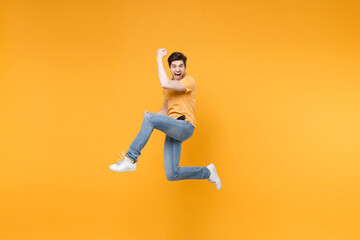 Fototapeta na wymiar Full length side view of young overjoyed excited surprised man in casual t-shirt jeans high jump up do winner gesture with clenching fists look camera isolated on yellow background studio portrait.