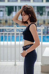 A girl stands on the street against the background of a building and a pool of water