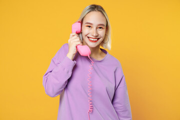 Young blonde smiling caucasian woman 20s bob haircut bright makeup wearing casual basic purple shirt talking by pink retro vintage handset phone isolated on yellow color background studio portrait.