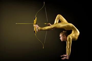 Archer Shooting by Legs mit goldenem Pfeil und Bogen. Flexible Turnerin, die auf ein Ziel zielt, das auf der Hand steht. Zielerreichungskonzept, Studioaufnahme auf schwarzem Hintergrund © inarik