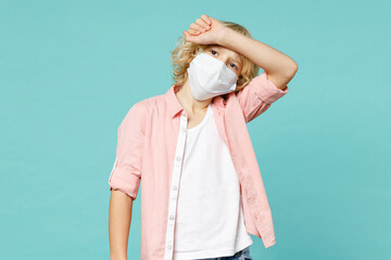 Sick little kid boy 10s in shirt sterile face mask safe from coronavirus virus covid-19 put hand on head isolated on blue turquoise background children studio portrait. Childhood lifestyle concept.