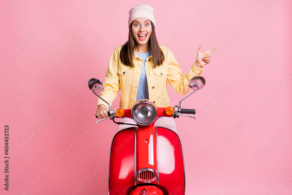 Sticker Photo of young happy excited crazy happy girl woman female point finger in copyspace ride red motorbike isolated on pink color background