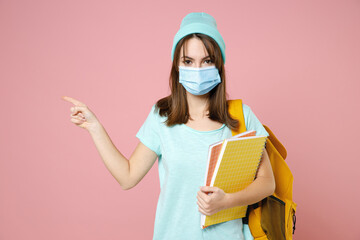Young woman student in t-shirt hat backpack face mask to safe from coronavirus virus covid-19 point index finger aside isolated on pink background. Education in high school university college concept.