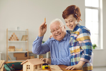 Happy old carpenter teaches little boy new handwork skills. Senior man with teen grandson have fun...