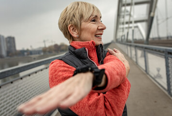 Active senior woman stretches her muscles before running through the city during the day.