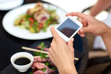 technology and people and concept - close up of couple with smatphone taking picture of food at restaurant terrace