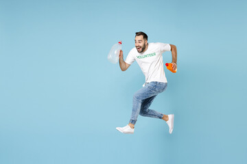 Full length of excited funny young man in volunteer t-shirt jumping running hold plastic bottles trash isolated on blue background. Voluntary free assistance help, trash sorting recycling concept.