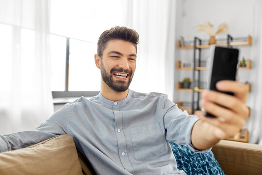 technology, people and lifestyle concept - happy man with smartphone taking selfie or having video call at home