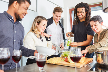 Lachende Freunde bereiten Salat vor für gemeinsame Mahlzeit in Küche