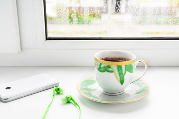 A cup of coffee, phone and headphones on the windowsill