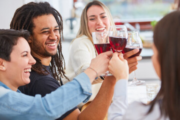Lachende Freunde stoßen zusammen zu Hause mit Glas Rotwein an