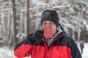 Fototapeta na wymiar A mug with a hot drink in the hands of a man. Portrait of a man for a walk in the winter forest.