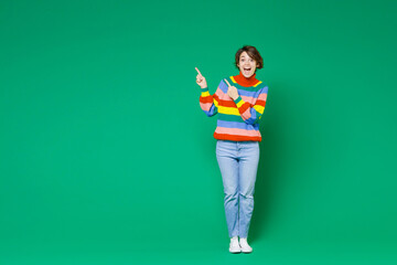 Full length of excited shocked young brunette woman 20s years old wearing basic casual colorful sweater stand pointing index fingers aside up isolated on bright green color background studio portrait.