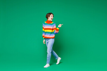 Full length side view of excited shocked young brunette woman 20s in basic colorful sweater pointing index finger aside on mock up copy space isolated on bright green color background studio portrait.