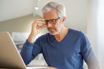 Senior man having migraine while working on laptop computer