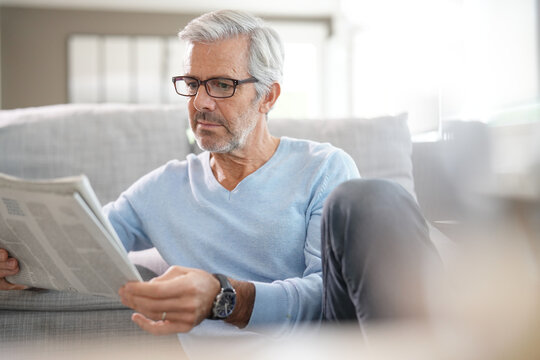 Attractive senior man with eyeglasses relaxing at home reading newspaper