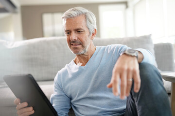 Fototapeta premium 60-year-old man at home connected with digital tablet