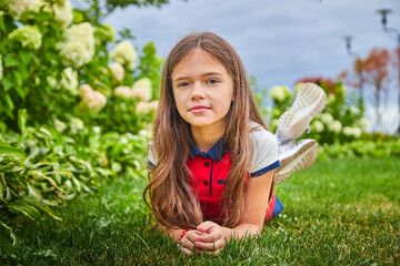 Young girl with long hair on the lawn with green grass and white flowers