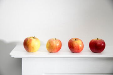 Four red apples are stands on a white mantel.