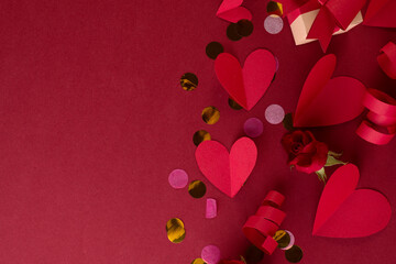 Red paper Hearts, festive decor, and confetti on a dark red background. Valentines Day monochrome border with empty space for text .