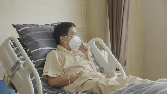 Asian man patient wearing face mask coughing and sneezing protective who lay down on hospital in recovery room after disease of Covid-19, State quarantine, Covid-19 pandemic concept.