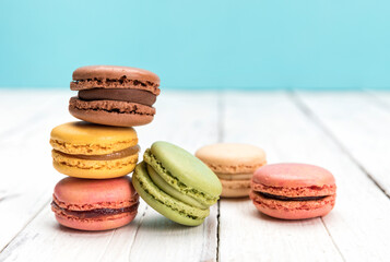 French macarons pastry variety with vanilla, coffee and chocolate flavours on rustic wooden surface, blue background