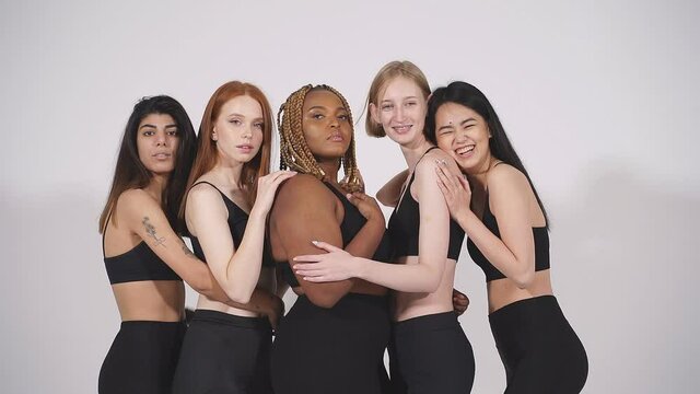 Interracial models hugging each other, having close friendship, posing at camera in bodysuit, isolated on white studio background.