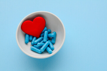 Blue medical capsules in white bowl and red heart on  blue background. Concept of prevention and treatment of cardiovascular diseases, Valentine's day. Medical flat lay. world pharmaceutical day