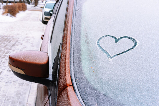 A heart painted on a frozen car window in winter
