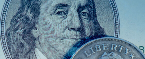 Close uup one hundred US Dollar and coin with description: Liberty. Selective focus on eyes of Benjamin Franklin