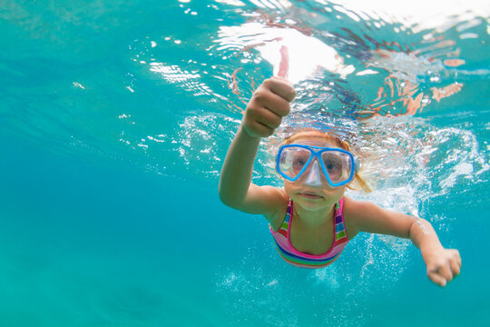 Photo of happy baby girl jump, dive underwater with fun in tropical lagoon pool. Travel lifestyle, water sport, snorkeling adventure. Family swimming lessons on summer sea beach vacation with kids