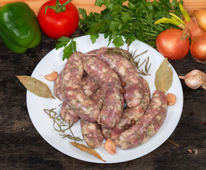 Uncooked homemade pork sausages on dish on black surface, semifinished