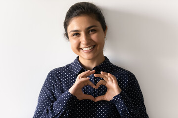 Headshot portrait of smiling young Indian woman isolated on grey studio background show heart love...