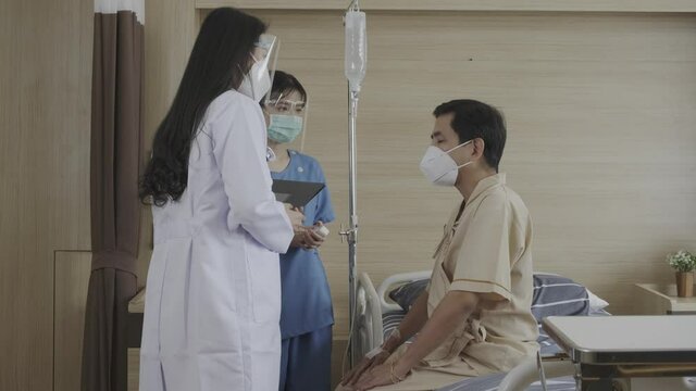 Asian doctor and nurse taking care of asian man patient wearing face mask protective who lay down on hospital in recovery room after disease of Covid-19, State quarantine, Covid-19 pandemic concept.