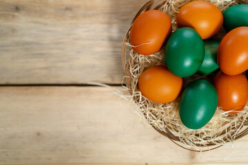 Wicker basket with orange and green Easter eggs on a dark wooden table close-up