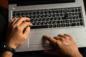Male hands with black smartwatch on wrist and wedding ring on finger typing on gray laptop keyboard top view