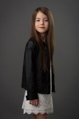 girl child with beautiful hair in a white dress and a black leather jacket on a gray background