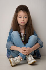 Fototapeta premium girl child with long hair in jeans and denim jacket posing sitting against a white wall